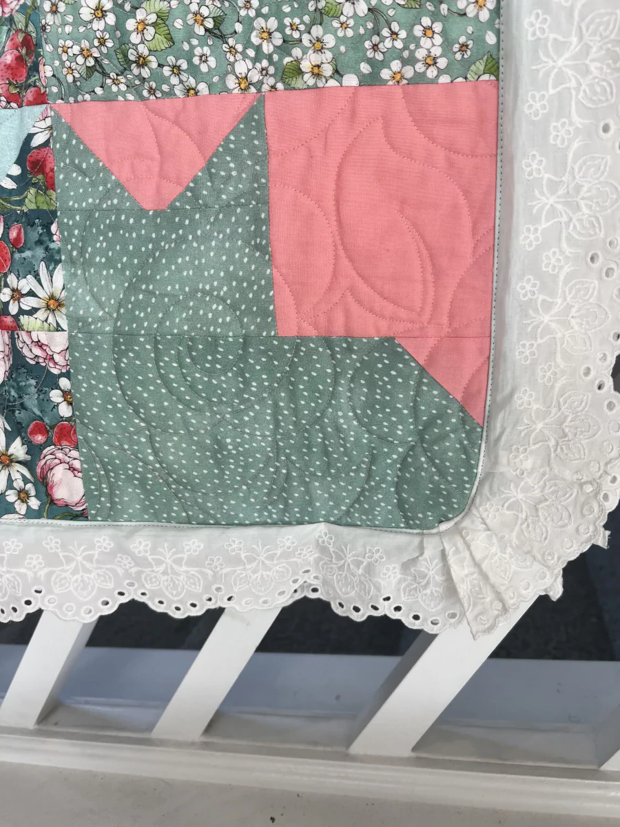 Quilted corner with pink and sage blocks beside white embroidered lace