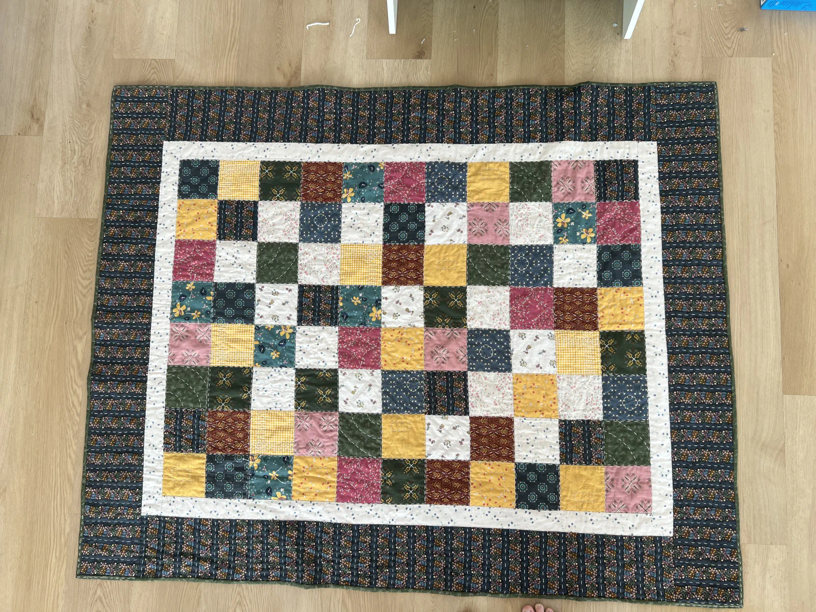 Rectangular patchwork quilt laid flat with a dark floral outer border